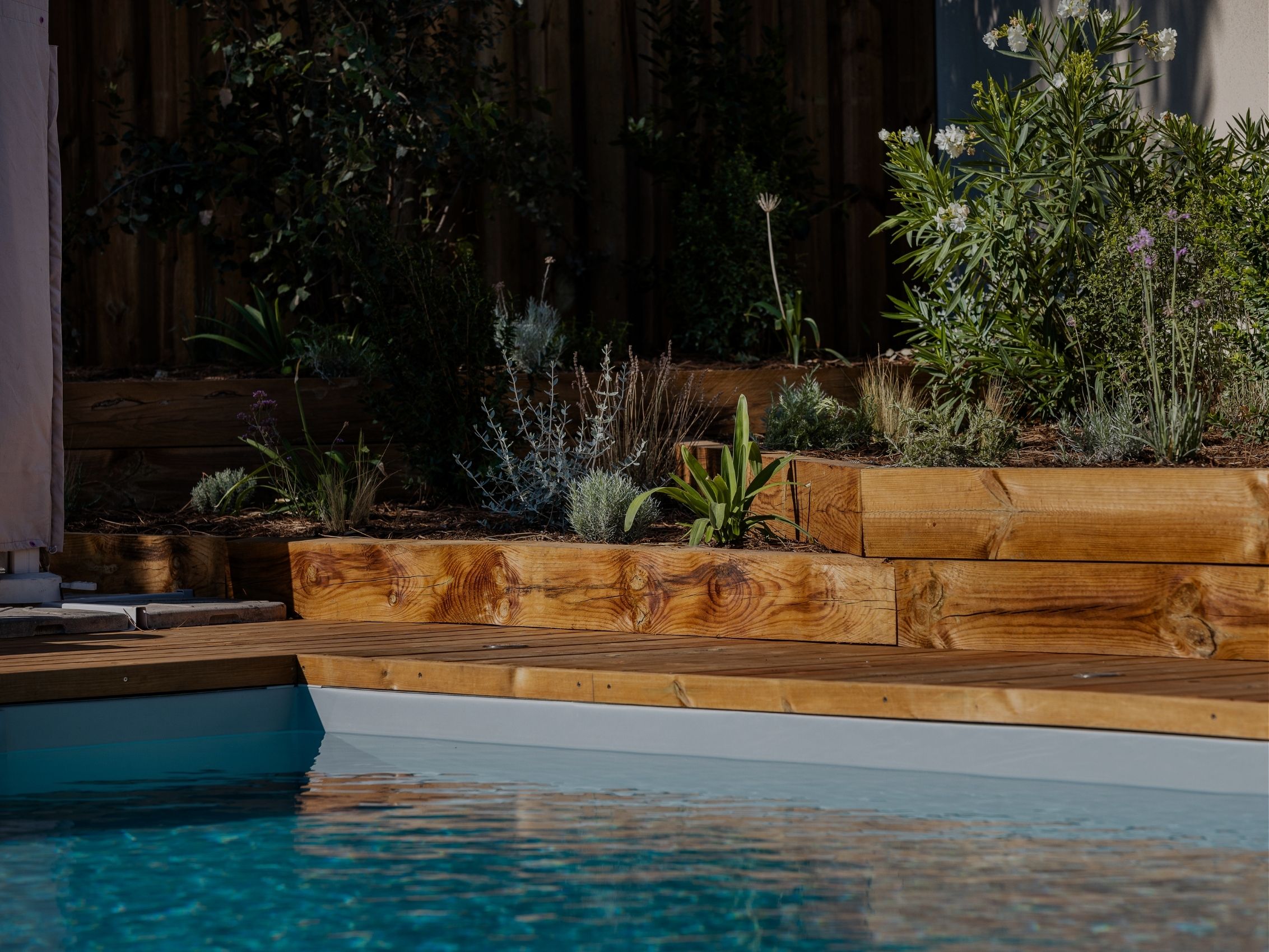 Jardinières en traverses de bois massif plantées de végétaux méditerranéens en bordure d'une piscine avec plage en bois, réalisation TO L'Atelier des Jardins, paysagiste à Bordeaux.